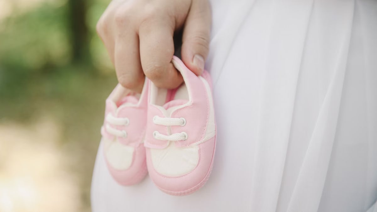 A close-up of a hand holding pink baby shoes, symbolizing new life and parenthood.